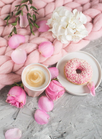 Cup with cappuccino, doughnut, pink pastel giant blanket, flowers, bedroom, morning conceptの写真素材