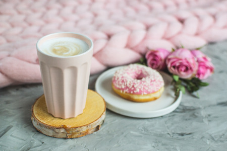 Cup with cappuccino, doughnut, pink pastel giant blanket, flowers, bedroom, morning concept