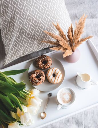 Breakfast in bed, cup with cappuccino, donuts, flowers white tulips, morning concept, linen bed sheets, woman's dayの写真素材