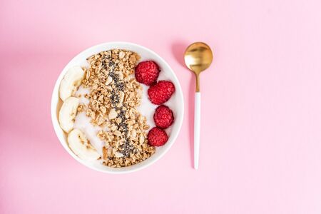 Yogurt with granola, chia seed, raspberry and banana, healthy breakfast concept, pastel pink background, top viewの写真素材