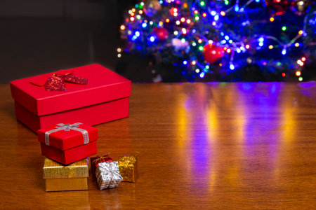 Red, yellow and silver Christmas present. On top of wooden table with background of Christmas trees.の写真素材