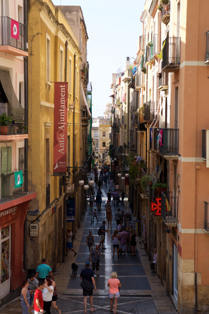 TARRAGONA, SPAIN - AUG 28th, 2017: Deserted street of old European town on a clear sunny day with many people walking. The bright walls of the old town of Tarragona in Cataloniaのeditorial素材