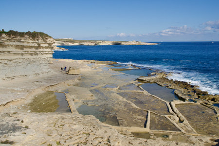 MARSAXLOKK, MALTA - 03 JAN, 2020: Traditional salt fields, Mediterranean Sea and small limestone hill in the background near Peters poolのeditorial素材