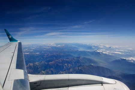 TURIN, ITALY - 13 SEP 2019: Aerial view above the clouds from a plane flying over the Swiss Alps, with mountain peaks covered in snow and a river flowing through the mountainsのeditorial素材