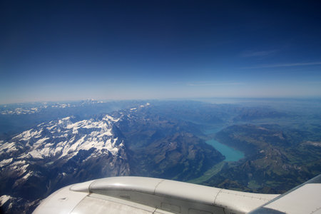 TURIN, ITALY - 13 SEP 2019: Aerial view above the clouds from a plane flying over the Swiss Alps, with mountain peaks covered in snow and a river flowing through the mountainsのeditorial素材