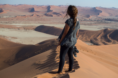 Woman Standing on Big Daddy Dune Looking onto Desert Landscape, Sossusvlei, Namibiaの写真素材