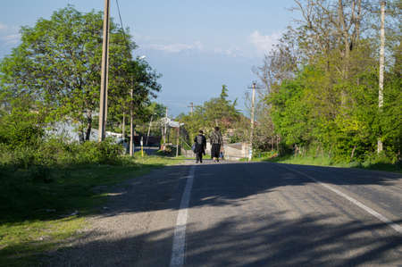 Two Women Walking down a Road in a Small Georgian Village near Sighnaghi with view onto the Caucasus Mountains, Georgiaの写真素材