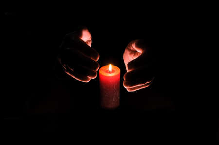Burning candle between the palms on a dark background.の写真素材