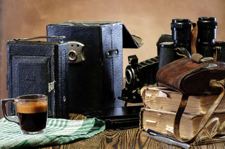 Stack of old books, binoculars, vintage camera, frayed leather cases on a wooden tableの写真素材