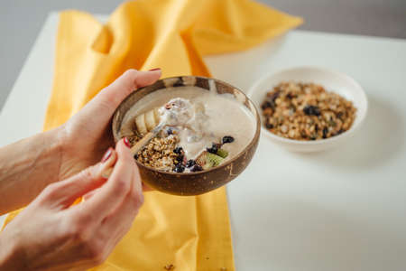 Woman holding plate coconut plate with tasty smoothie bowl. Berries, fresh kiwi and banana in oatmeal. Close up. Healthy food and tropical style. Healthy food conceptの写真素材