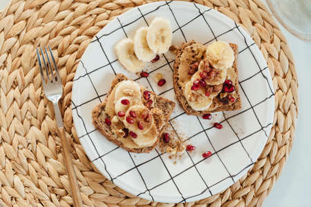 Peanut butter toast with banana slices and pomegranate on plate. Healthy breakfast, flat layの写真素材