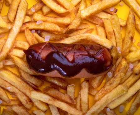 The ketchup sausage is on the fries. Yellow bright background. Food background. View from above.の写真素材