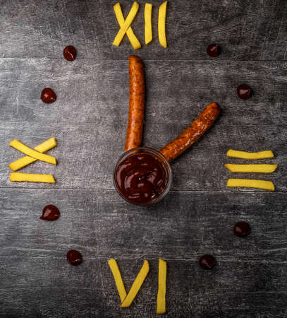 A clock made of fries, ketchup sausages. Lunch time. Creativity.の写真素材
