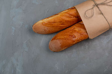 Freshly baked baguettes in a paper bag on a gray texture background.