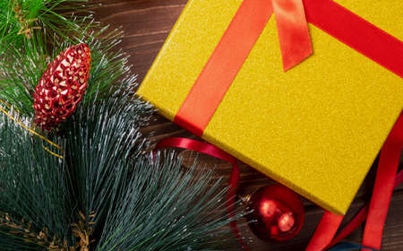 Festive tree with toys and a gold box with a red ribbon and a gift, close-up.