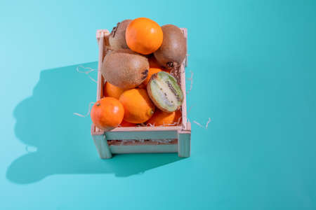 Wooden box with fruits. Tangerines, kiwi in a wooden box on a blue background. View from above. Hard lightの写真素材