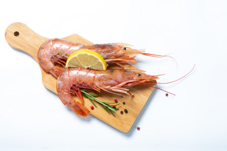Two shrimps with lemon and rosemary on a cutting board. White background. View from above.