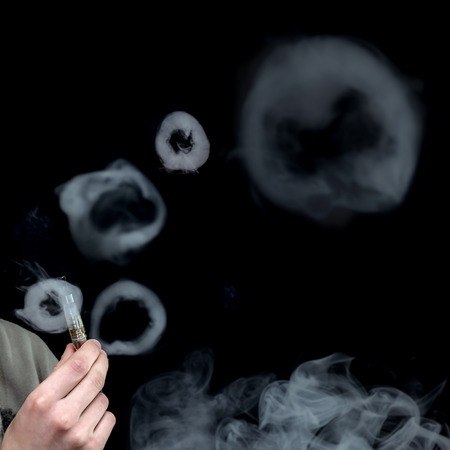 Electronic Cigarette Smoke in Circles over Black Background, Selective focus on hand holding e-cigaretteの写真素材