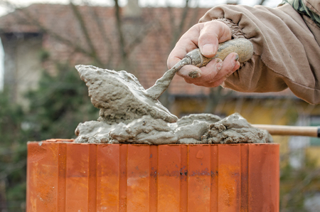 Bricklayer worker installing brick masonry on exterior wall with trowel putty knifeの写真素材