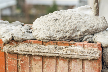 Bricklayer worker installing brick masonry on exterior wall with trowel putty knifeの写真素材
