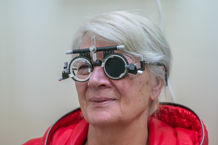 Zrenjanin, SERBIA, February 2018: Elderly woman wearing phoropter or trial frame and looking at mirrored eye test chart during sight test at optometric.のeditorial素材