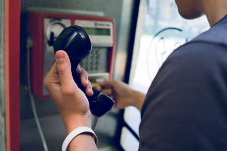Close up on hand of a young man holding a phone at public call boxの写真素材