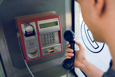 Close up on hand of a young man holding a phone at public call box