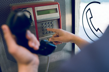 Close up on hand of a young man holding a phone at public call box dialing numberの写真素材