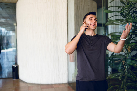Young man using mobile phone smiling talking by the building at city