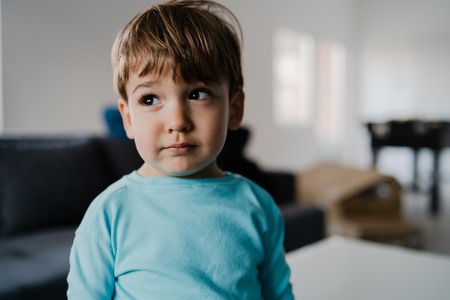 Portrait of a little boy in blue at home standing in the middle of the roomの写真素材