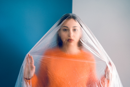 Portrait of young woman in orange in front of blue wall covered with nylon plastic bag, antipollution pollution save the planet oceans conceptの写真素材