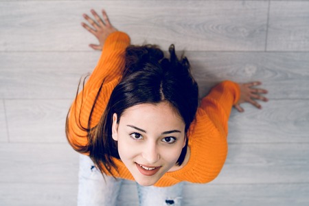 High angle view of beautiful young woman in orange sitting on the floor looking up to the cameraの写真素材