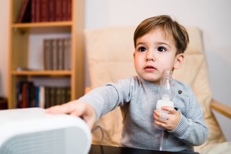 Little boy using steam inhaler nebulizer mask inhalation at home. Medical procedures vapor medication treatment asthma pneumonia bronchitis coughingの写真素材