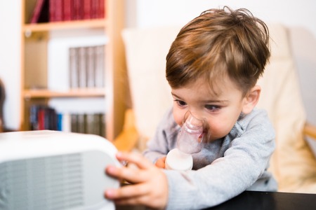 Little boy using steam inhaler nebulizer mask inhalation at home. Medical procedures vapor medication treatment asthma pneumonia bronchitis coughingの写真素材