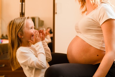 Little girl at home standing by the mother pregnant woman waiting excited for the baby brother or...