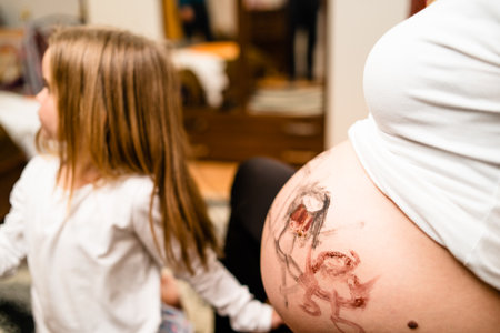 Little blonde girl painting little baby brother or sister on her mothers pregnant belly with water colorsの写真素材