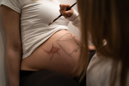 Little blonde girl painting on her mothers pregnant belly with water colorsの写真素材