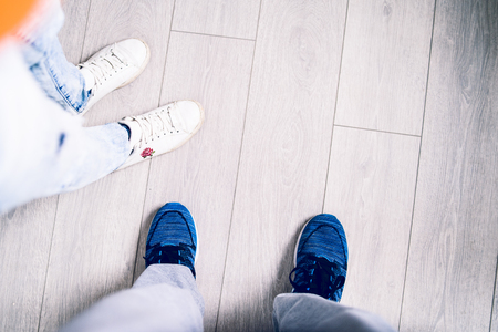 High angle view on man's and woman's sneakers shoes feet standing on the wooden floor at homeの写真素材