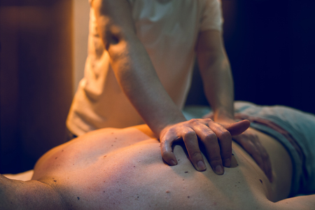 Young woman female massage therapist giving massaging relax sport to young athlete at spa studioの写真素材