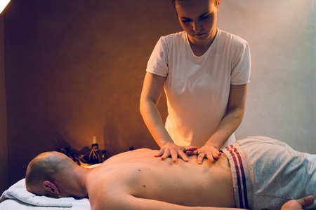 Young woman female massage therapist giving massaging relax sport to young athlete at spa studioの写真素材