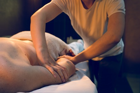 Young woman female massage therapist giving massaging relax sport back to young athlete at spa...