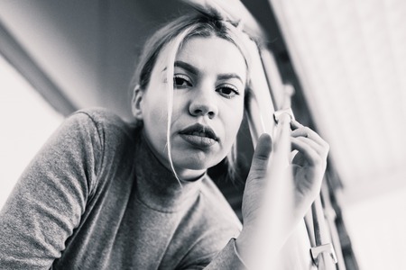 Portrait of beautiful young woman with blonde hair looking to the camera sitting on the stairs at home black and whiteの写真素材