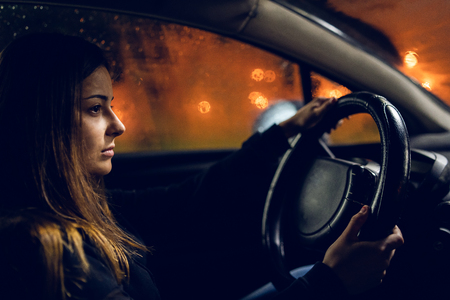 Young woman holding a car driving wheel in a rainy night rainの写真素材