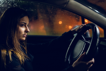 Young woman holding a car driving wheel in a rainy night rainの写真素材