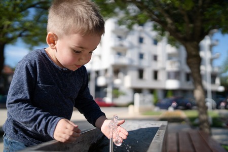 Little boy at the public fountain playing with water drinking in summer sunny dayの写真素材