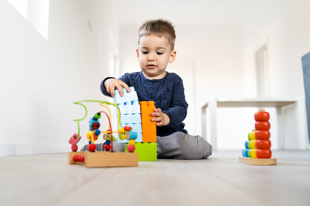 Small boy playing with plastic brick block toys on the wooden floor at homeの写真素材