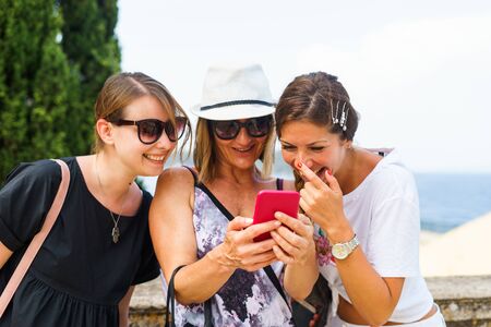 Three woman looking to the smart-phone mobile phone searching for the tourist information photos in...