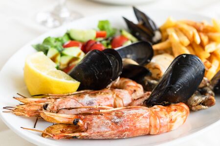 Seafood meal on the white dish plate cooked mussels shrimp or prawns with lemon and vegetables...
