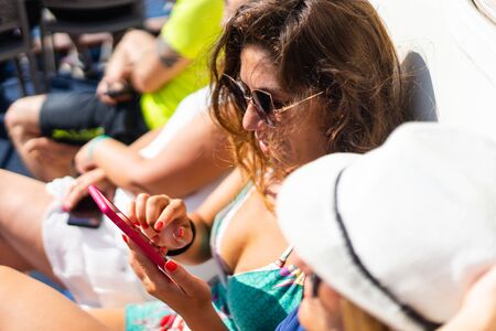 Two women using mobile phone on the ship in summer day looking at the pictures sending and reading...