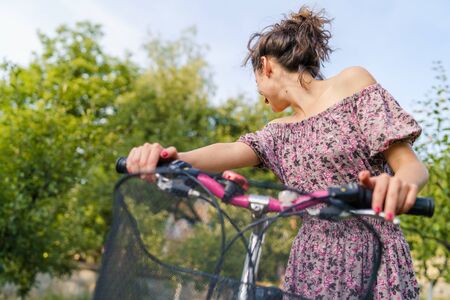 Young woman holding handlebar grip driving pushing bicycle in a summer sunny day wearing dress in nature countryside outdoorの写真素材